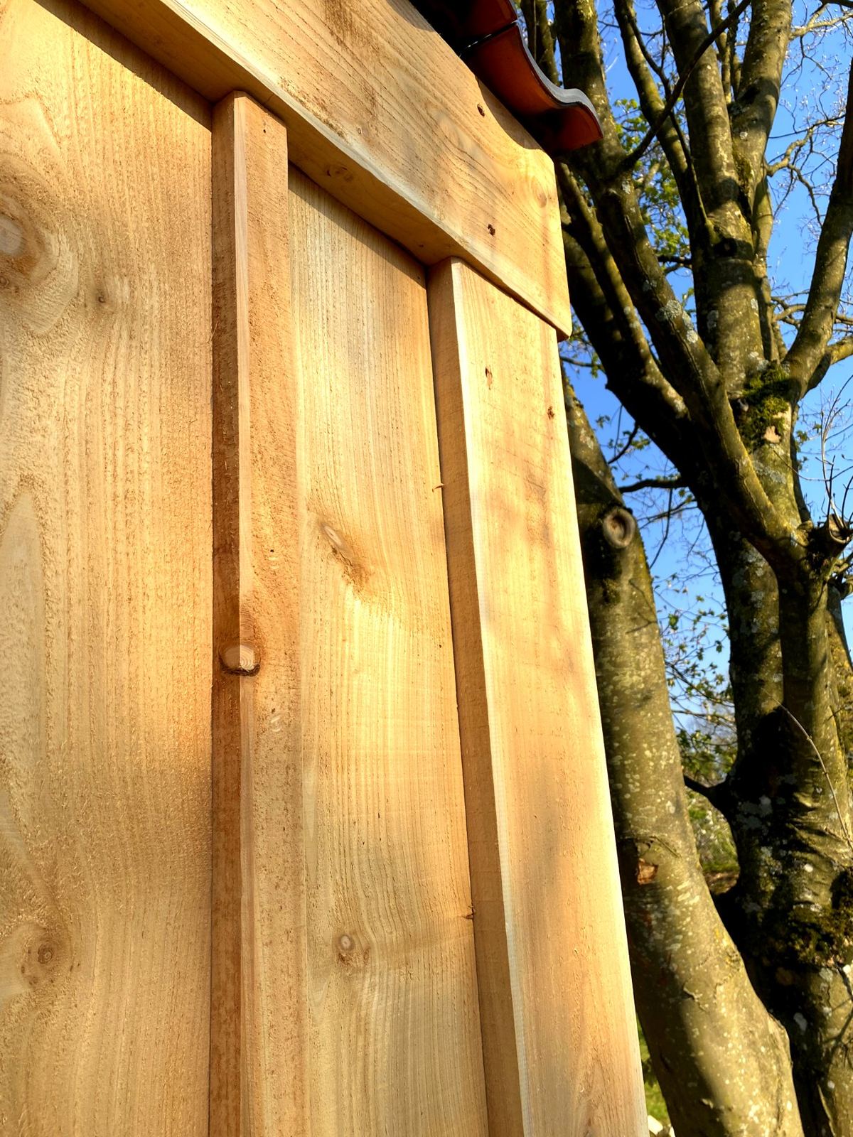 Batten-over-board cedar cladding under a shaped fascia, with a tree and blue sky behind
