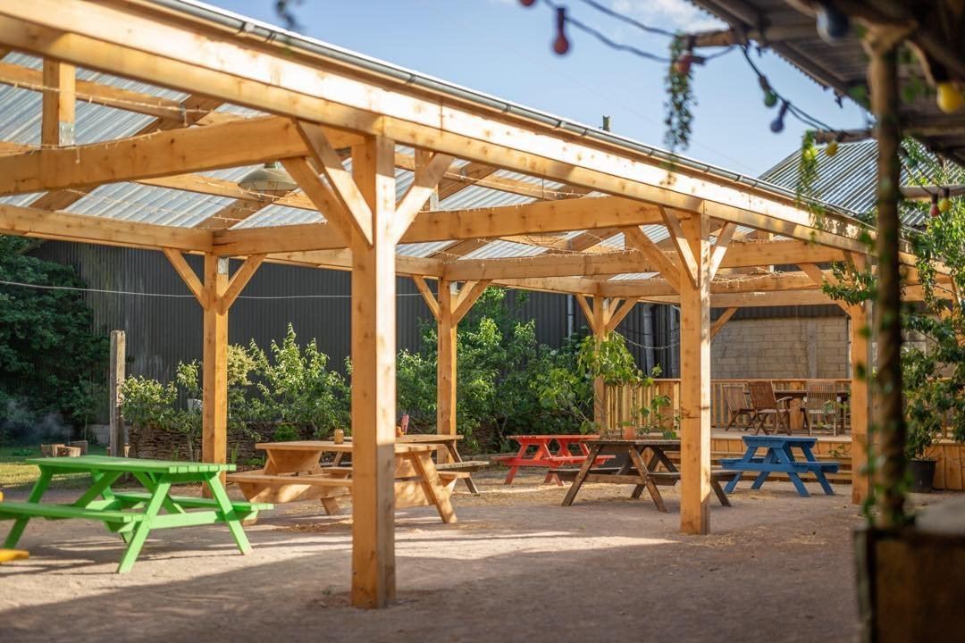 Open timber canopy with knee-braced posts over picnic tables in a pub garden