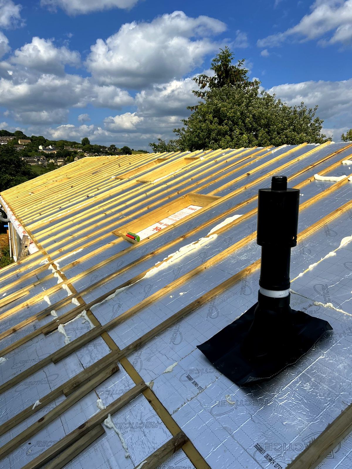 New insulated roof with battens, a rooflight opening and a flue, looking out over Stroud