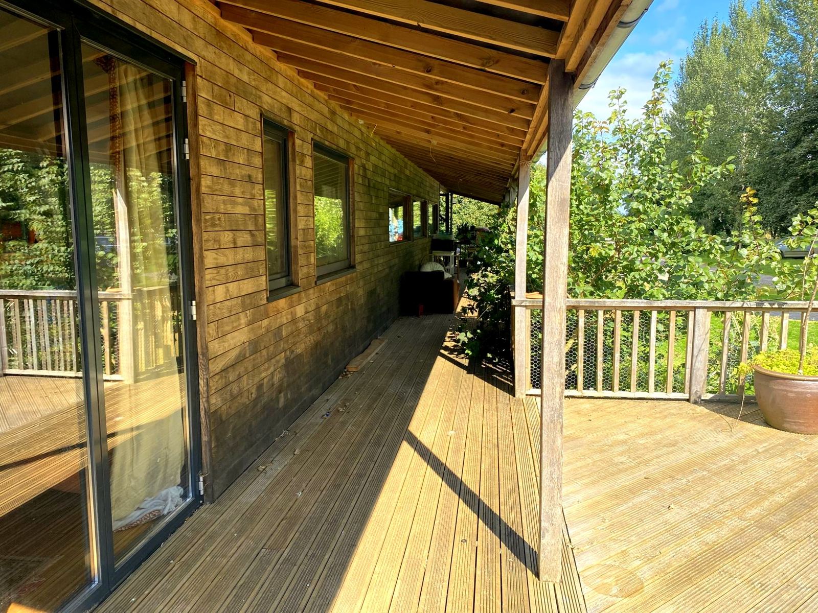 Timber-clad house with a long covered veranda on oak posts and a raised deck