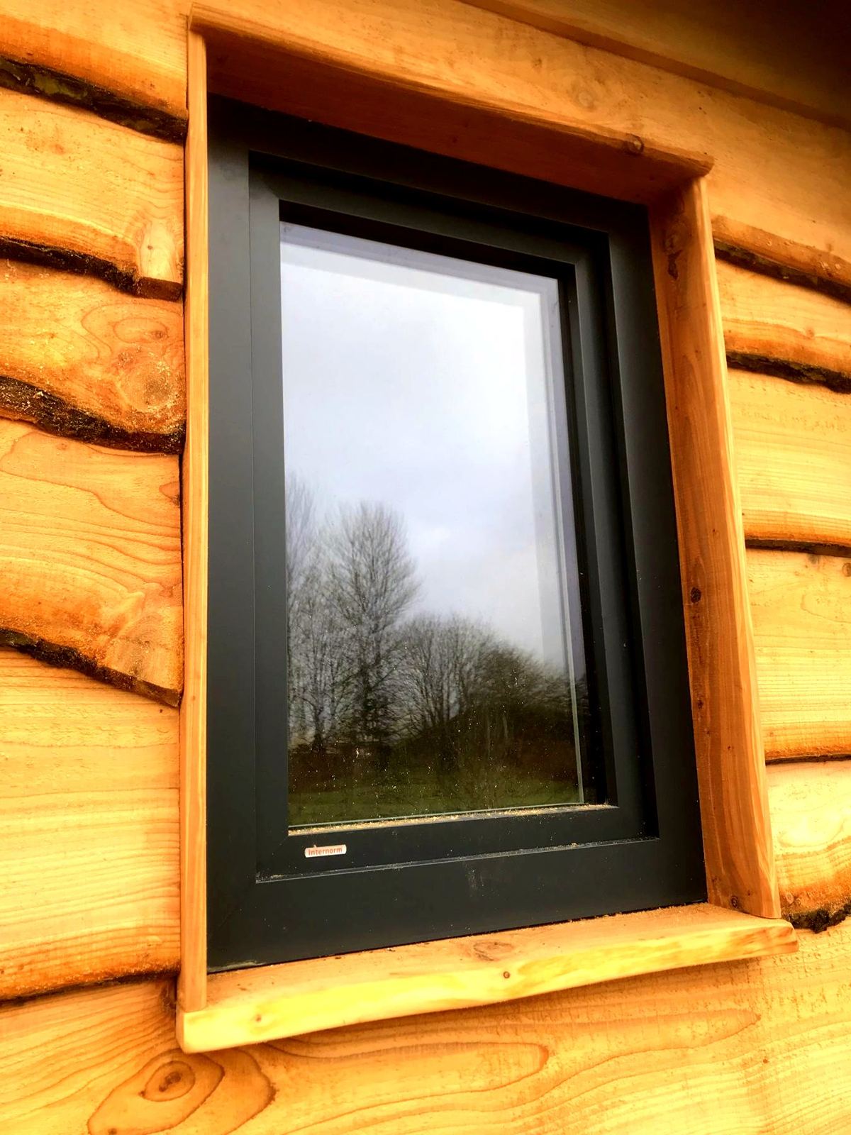 Dark-framed window with a timber surround in waney-edge cladding