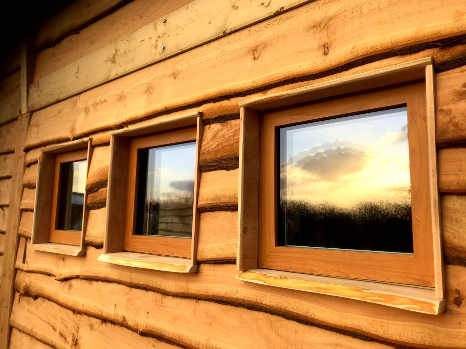 Three small square windows in timber cladding at sunset